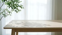Wooden table with natural light casting leaf shadows from potted plant, minimalist interior design workspace for product display and styling.