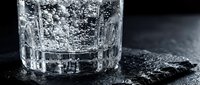 Crystal clear sparkling water in textured glass tumbler on dark wet surface with dramatic lighting for beverage and refreshment concepts.