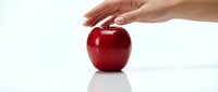 Young adult Caucasian hand reaching toward glossy red apple on white surface, symbolizing healthy eating, nutrition, and wellness choices for lifestyle and diet concepts.