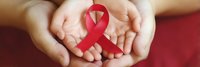 Hands holding red AIDS awareness ribbon, symbolizing support and solidarity for HIV/AIDS prevention and education.