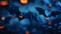 Flying black bats with glowing orange eyes against dark blue night sky, blurred jack o'lantern lights in background create spooky Halloween atmosphere.
