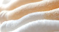 Soft white and beige fluffy towel texture in macro shot showing cotton fabric fibers and gentle folds creating abstract waves and curves in natural light.
