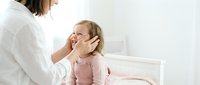 Mother gently touching daughter's face in tender moment on white bed. Loving parent-child bonding scene in bright bedroom setting for family content.