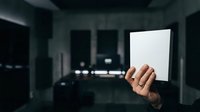 Person holding blank white card in dark modern office space with blurred background lights and contemporary interior design.