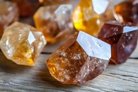 Raw brown and honey colored crystals of natural mineral stones scattered on rustic wooden surface with soft lighting highlighting their translucent facets.