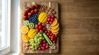 Colorful fresh fruit and vegetable platter with nuts on wooden cutting board. Healthy organic food arrangement for meal prep and nutritious snacking.