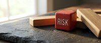 Red wooden cube with RISK text among fallen wooden blocks on slate surface, symbolizing financial danger, business uncertainty and investment challenge.
