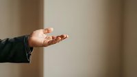 Man's hand in open palm gesture against neutral beige wall background, conveying offering, acceptance, or presentation for business and communication concepts.