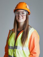 Young Caucasian female construction worker wearing orange hard hat, safety glasses, and high visibility vest smiles confidently against gray background. Professional portrait.