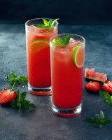 Refreshing watermelon cocktails garnished with lime slices, fresh mint leaves and ice cubes on dark background. Fresh strawberries and mint as decoration.