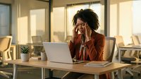 Young African American businesswoman experiencing stress and headache while working on laptop in modern office during golden hour sunset.