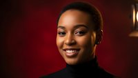 Professional African American businesswoman smiling confidently in black turtleneck against warm red background for corporate marketing materials.