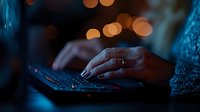Hand on laptop keyboard with warm bokeh lights in background, representing digital work, technology, programming, coding, online business, remote work, and cybersecurity concepts.