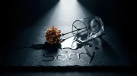 Dried rose and overturned empty glass on dark slate with the word Sorry written in spilled water, evoking regret, loss, and apology.