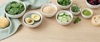 Healthy organic ingredients in white bowls on wooden table including spinach, quinoa, avocado, cucumber and berries for clean eating meal preparation.