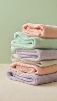 Stack of folded soft pastel colored towels on beige surface against light green background, showcasing spa-like bathroom textiles.
