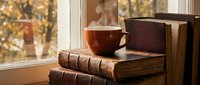 Steaming cup of hot tea or coffee resting on vintage books by a sunlit window in warm autumn atmosphere, cozy reading concept.