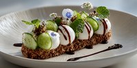 Gourmet dessert with white cream, cucumber slices, edible flowers and chocolate sauce on textured plate. Fine dining restaurant presentation for culinary arts.