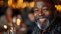 Smiling mature African American man with gray beard enjoying evening celebration with warm bokeh lights creating festive atmosphere for lifestyle content.