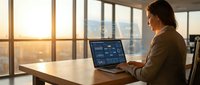 Professional businesswoman analyzing financial data on laptop in modern office with city skyline view during golden hour sunset for corporate presentations.