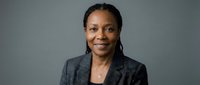 Professional African American businesswoman in gray suit smiling confidently against neutral background for corporate headshot and business presentations.