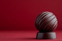 Dark chocolate truffle with elegant striped texture on a rich red background, perfect for luxury confectionery and gourmet dessert concepts.