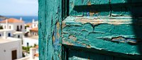 Weathered turquoise wooden shutter with peeling paint in Mediterranean coastal setting, showing aged texture and rustic charm for travel and architecture design projects.