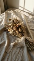 Dried wildflower bouquet tied with linen ribbon on soft fabric in warm sunlight, rustic boho wedding or home decor styling.