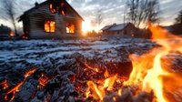 Dramatic scene of burning house in winter landscape with glowing flames and embers in snow at sunset, creating intense contrast between fire and frozen ground.