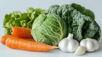 Fresh organic vegetables on light background - cabbage head, kale leaves, carrots, garlic bulbs and cloves arranged in rustic composition for healthy cooking.