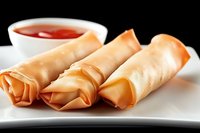 Crispy spring rolls served on white plate with sweet chili dipping sauce, close up view against dark background showing texture and golden brown color.
