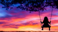 Silhouette of young girl on swing against dramatic sunset sky with vibrant pink, purple and orange clouds. Perfect for concepts of childhood, dreams, and freedom.