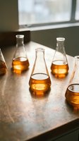 Laboratory flasks containing amber liquid arranged on a concrete surface near a window, suitable for scientific research, chemistry education, and pharmaceutical industry applications.