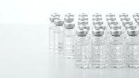 Medical glass vials arranged in rows on white background for pharmaceutical research and vaccine development in laboratory setting.