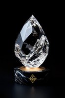 Crystal teardrop shape on luxurious black marble and gold pedestal against dark background, featuring geometric ornament and dramatic lighting effects.