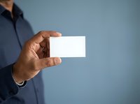 Male professional with dark skin tone wearing navy blue shirt holding blank white business card against blue background for corporate branding.