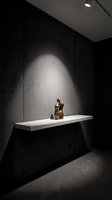 Modern minimalist interior with bronze sculpture on white floating shelf against dark wall with dramatic spotlight illumination for contemporary home decor.