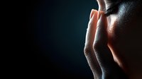 Person touching temple area showing stress, anxiety or headache against dark background with dramatic side lighting creating emotional mood and contrast.