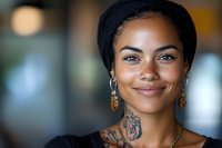Young African American woman with tattoos and gold earrings smiling confidently at camera in modern urban setting for lifestyle and portrait photography.