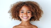 Young African American girl with curly natural hair and bright smile against white background, expressing joy and confidence in casual portrait.