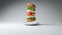 Deconstructed burger with floating ingredients including bun, lettuce, tomato and patty on white plate against gray background for food advertising.