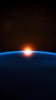 Sunrise over Earth horizon from space showing glowing atmosphere and stars against dark cosmos background. Dramatic orbital view of planet surface.