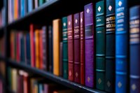 Row of vintage hardcover books with colorful spines in blue, purple, and red arranged neatly on dark wooden library shelf, selective focus creating depth and atmosphere.