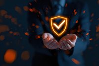 Glowing shield with checkmark hovering over outstretched hands against dark background with orange sparks, symbolizing digital protection and cybersecurity.