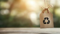 Recycling symbol on kraft paper tag with twine bow hanging against blurred natural background, eco-friendly concept for sustainable lifestyle and zero waste.