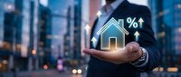 Professional businessman holding glowing house icon with percentage symbol in urban cityscape background for real estate investment and mortgage concepts.