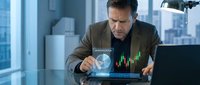 Middle-aged man with dark hair and facial hair, Caucasian ethnicity, wearing business casual attire, analyzing financial data and stock market charts on a holographic display in a modern office with city skyline views.