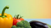 Fresh organic vegetables including yellow bell pepper, red tomato, green broccoli and purple eggplant arranged on pastel gradient background for healthy eating.