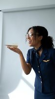 Smiling African American flight attendant in navy uniform holding coffee cup in modern aircraft cabin interior for hospitality service concepts.