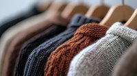Cozy knitted winter sweaters in neutral colors hanging on wooden hangers, showcasing texture and warmth. Closet organization and seasonal fashion concept.